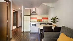 A compact kitchen with a microwave, oven, and modern stove. A dining area with a table and chairs is visible, and a plant is placed on the table. - SG Marina 54 Apartments (Castelldefels)