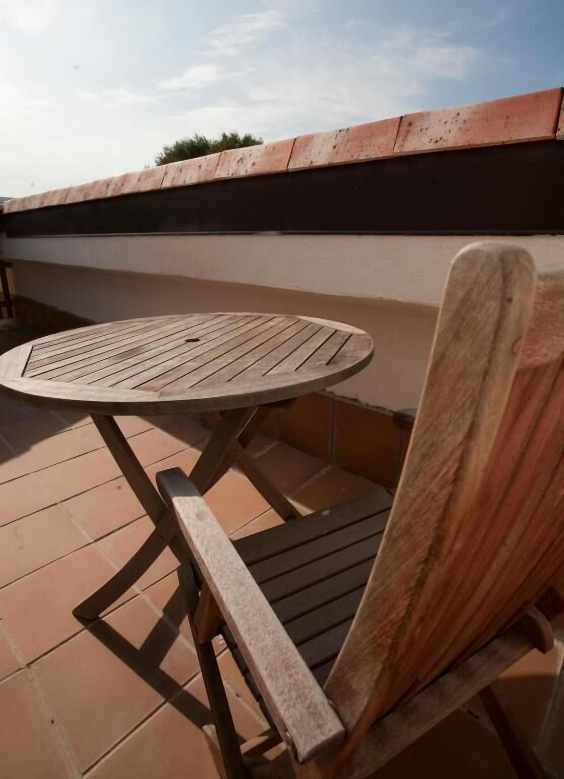 Una mesa redonda de madera y una silla de madera en un patio con baldosas.