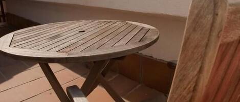Una mesa redonda de madera y una silla de madera en un patio con baldosas.