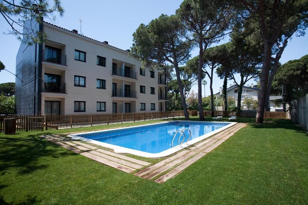 A modern apartment building with a swimming pool, surrounded by a wooden fence and trees.