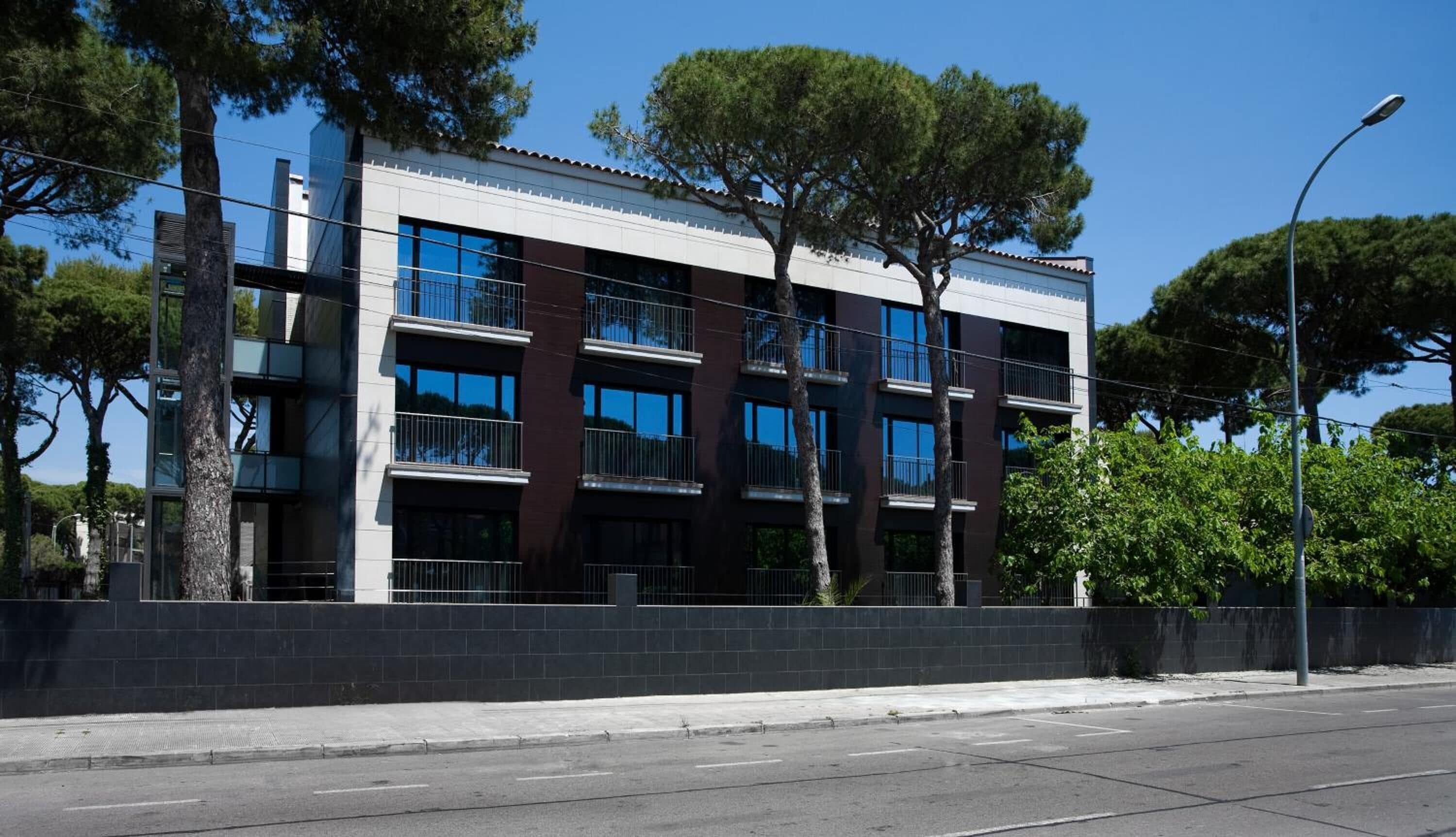 Un edificio moderno de varios pisos con balcones, cielo despejado y árboles.