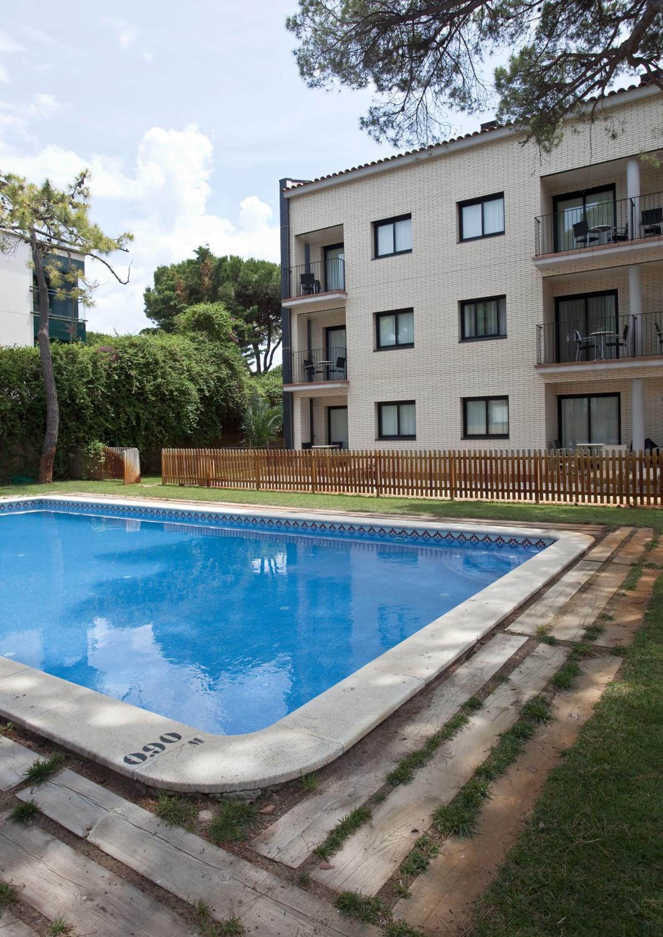 A rectangular swimming pool with a tiled edge, surrounded by a wooden deck and a low brick wall.