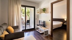 A modern hotel room with a sofa, a TV on a stand, a bed, and a small table. - SG Marina 54 Apartments (Castelldefels)