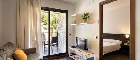 Quarto de hotel moderno com sofá, televisão em suporte, cama e mesa pequena.