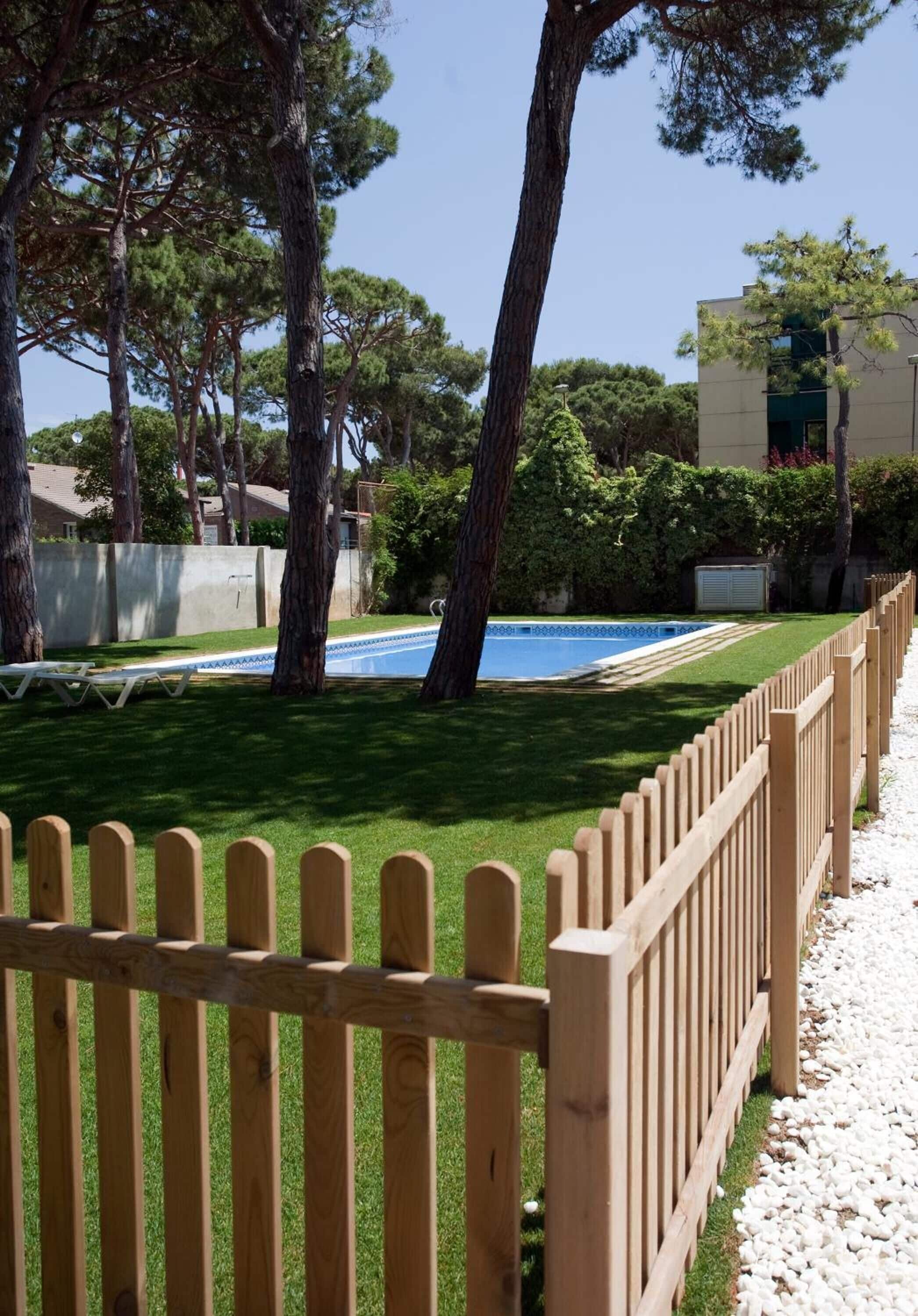Una zona de piscina con cerramiento de madera, césped verde y árboles.
