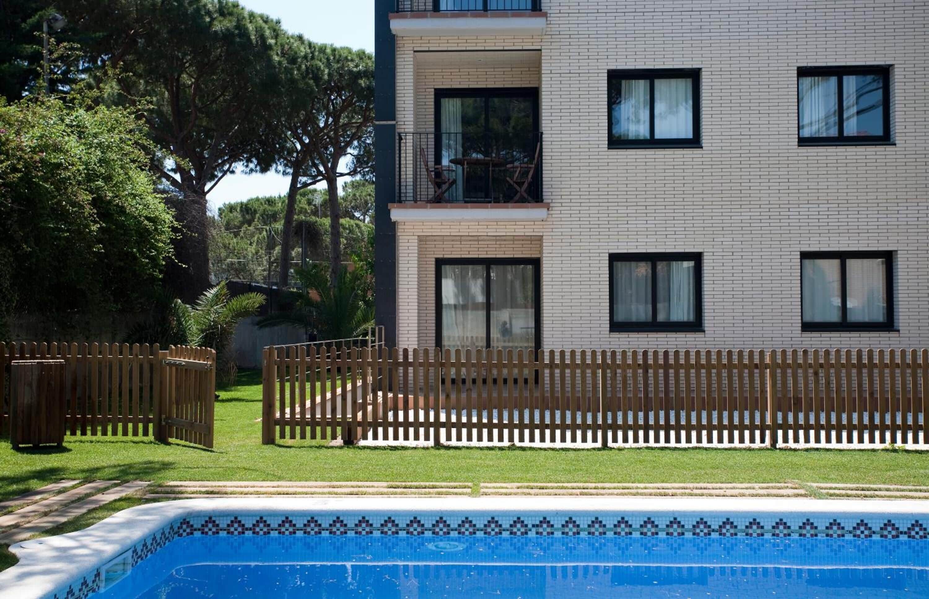 A modern two-story building with a brick facade, a balcony with outdoor furniture, and a swimming pool with a tiled border.