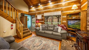 A cozy living room with a wooden staircase, a leather sofa, a television, and a fireplace.