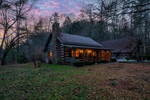 Situated in a wooded area, this cabin features a porch with a railing and a grassy yard.