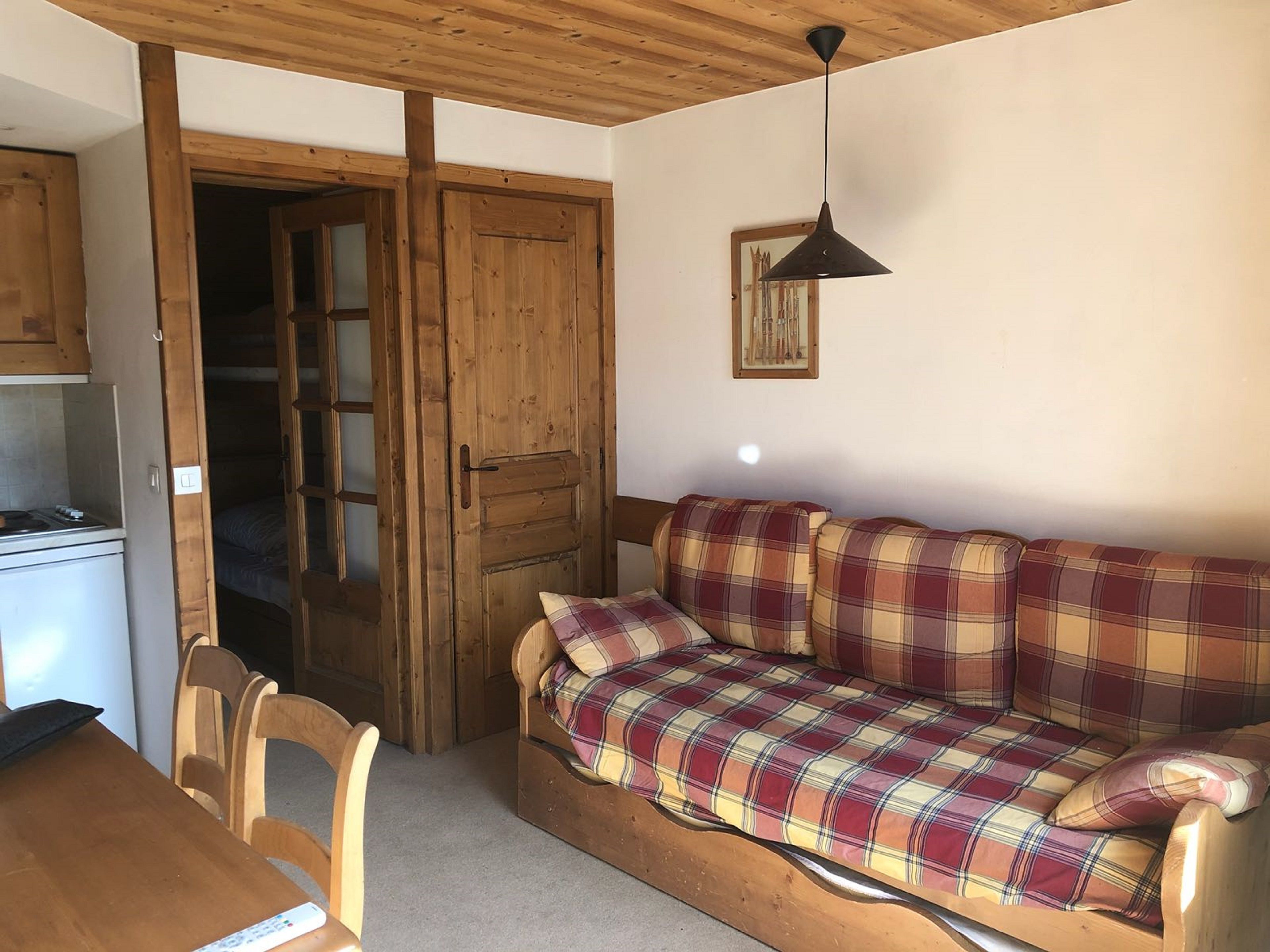 A cozy room with a wooden sofa, a dining table with chairs, and a kitchenette.