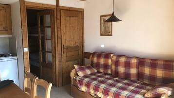 Una habitación acogedora con un sofá de madera, una mesa de comedor con sillas y una kitchenette.