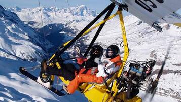 A person in a yellow and black ski lift chair with a snowy mountain landscape in the background.
