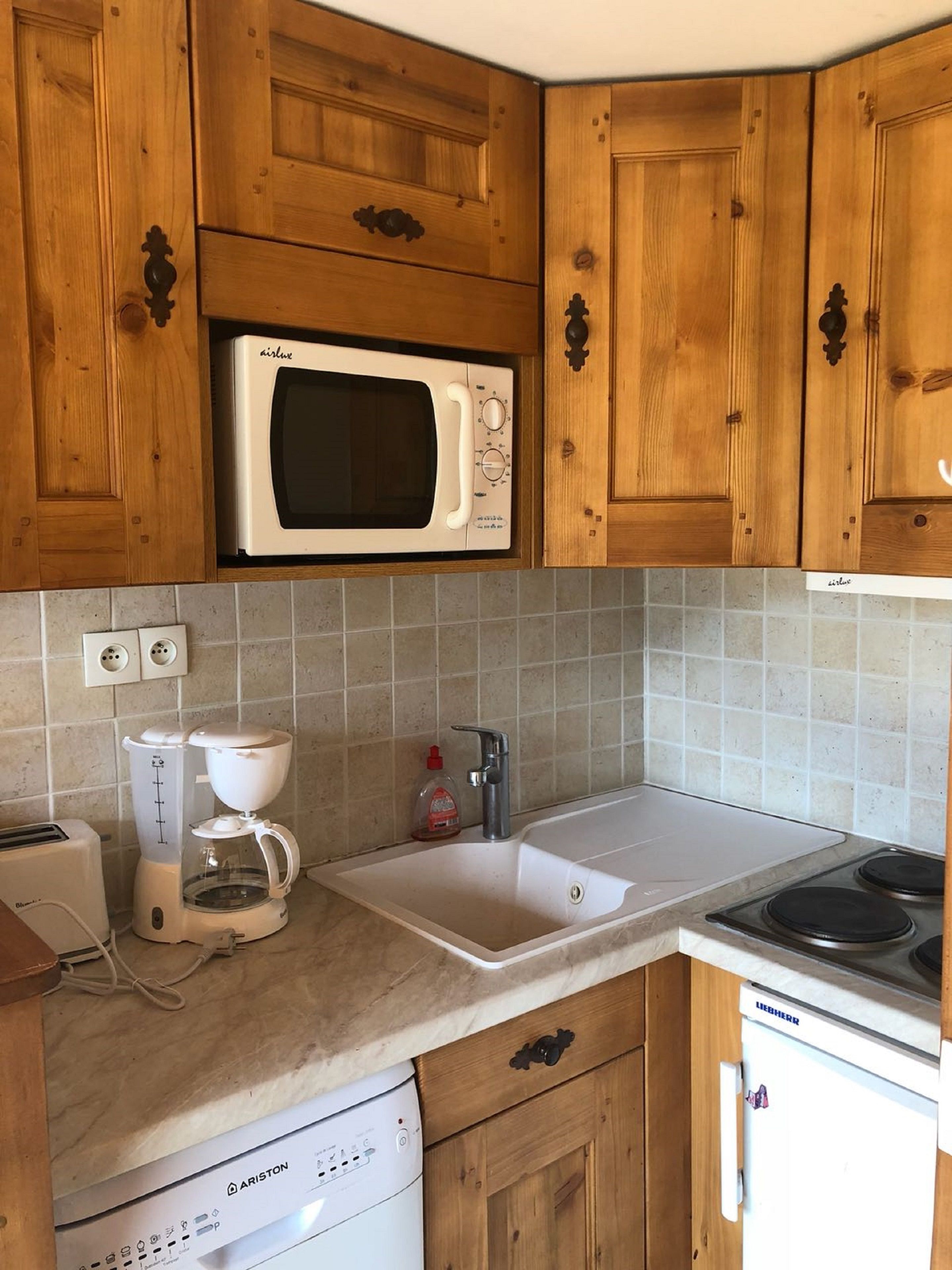 Ett kompakt kök med träskåp, en inbyggd mikrovågsugn, en kaffebryggare, ett handfat och en diskmaskin.