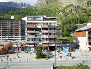 A multi-story building with balconies, a central open area with shops, and a mountainous backdrop. - Résidence Les Cîmes - Centre Val d'Isère (Val-d'Isere)