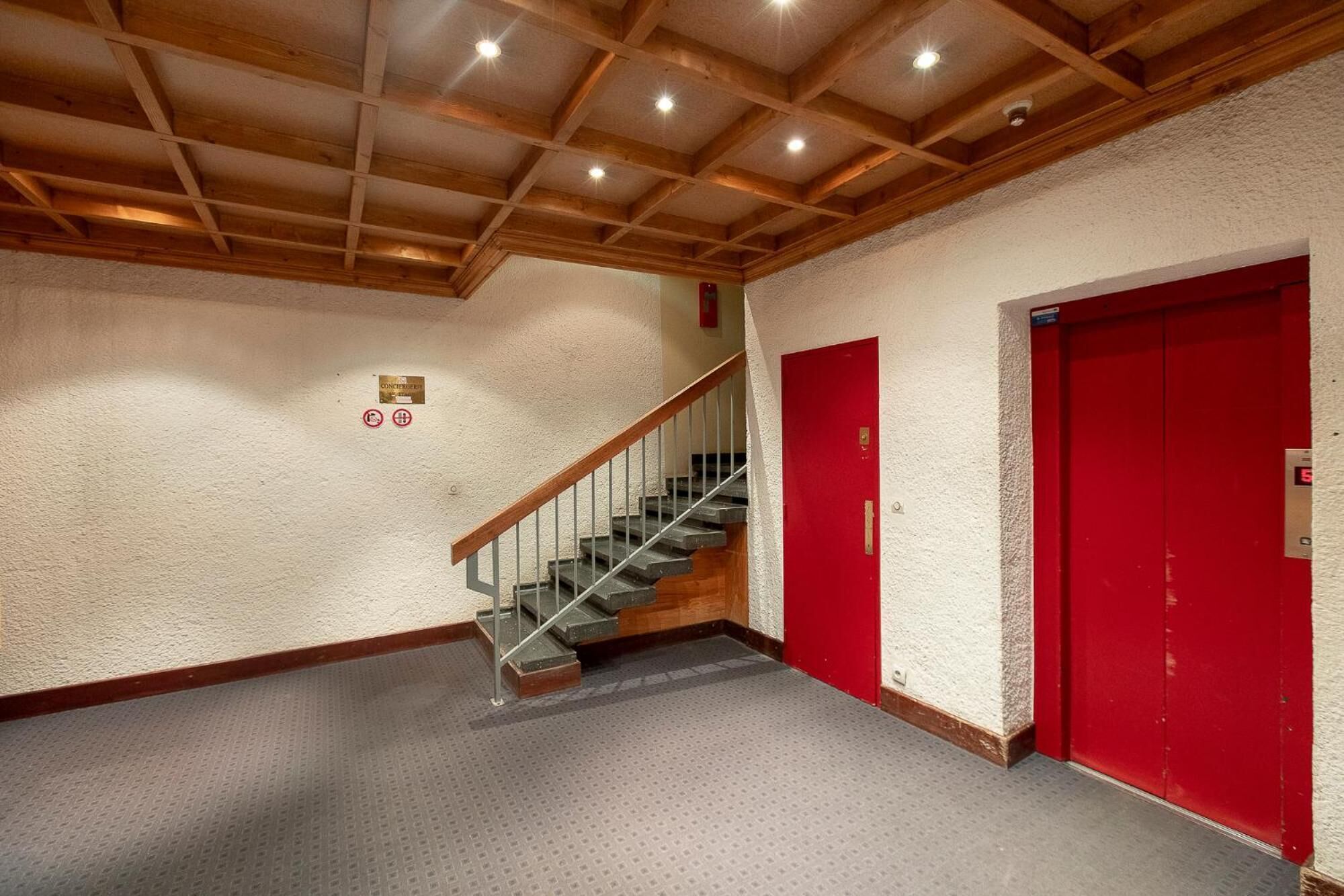 A hallway with a wooden ceiling, a staircase, and red doors.