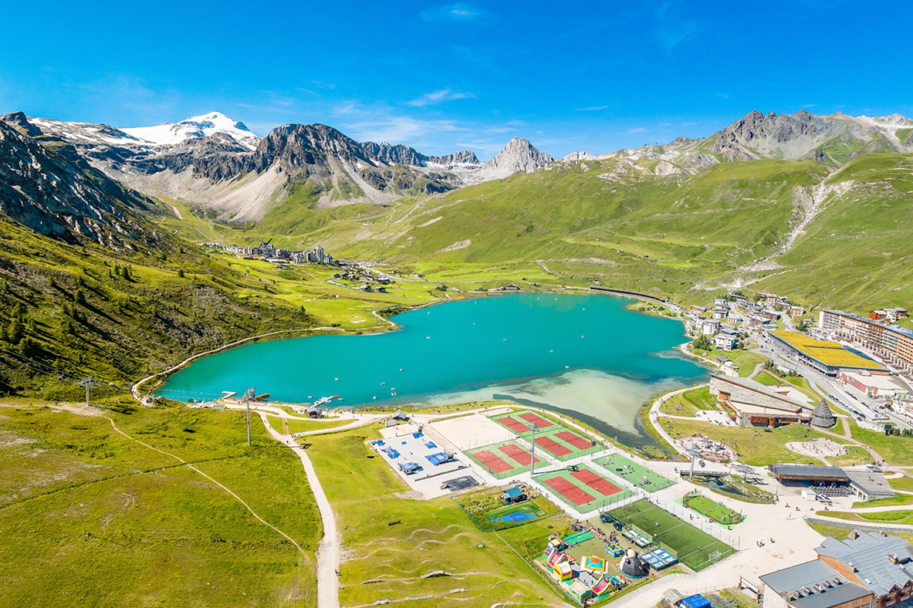 An aerial view of a mountainous area with a large turquoise lake, a ski resort, and a small town with buildings and roads.