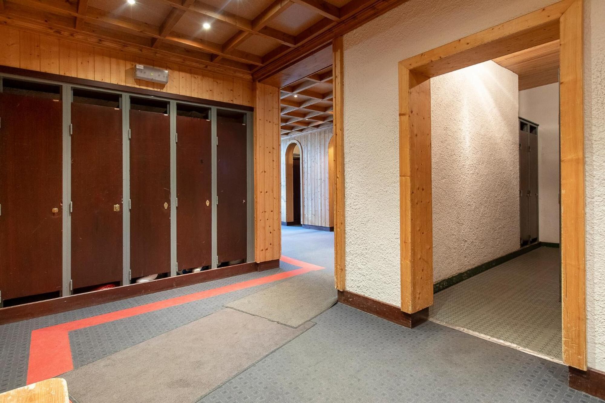 Un couloir avec des casiers en bois, un chemin tactile rouge et un mur à texture.