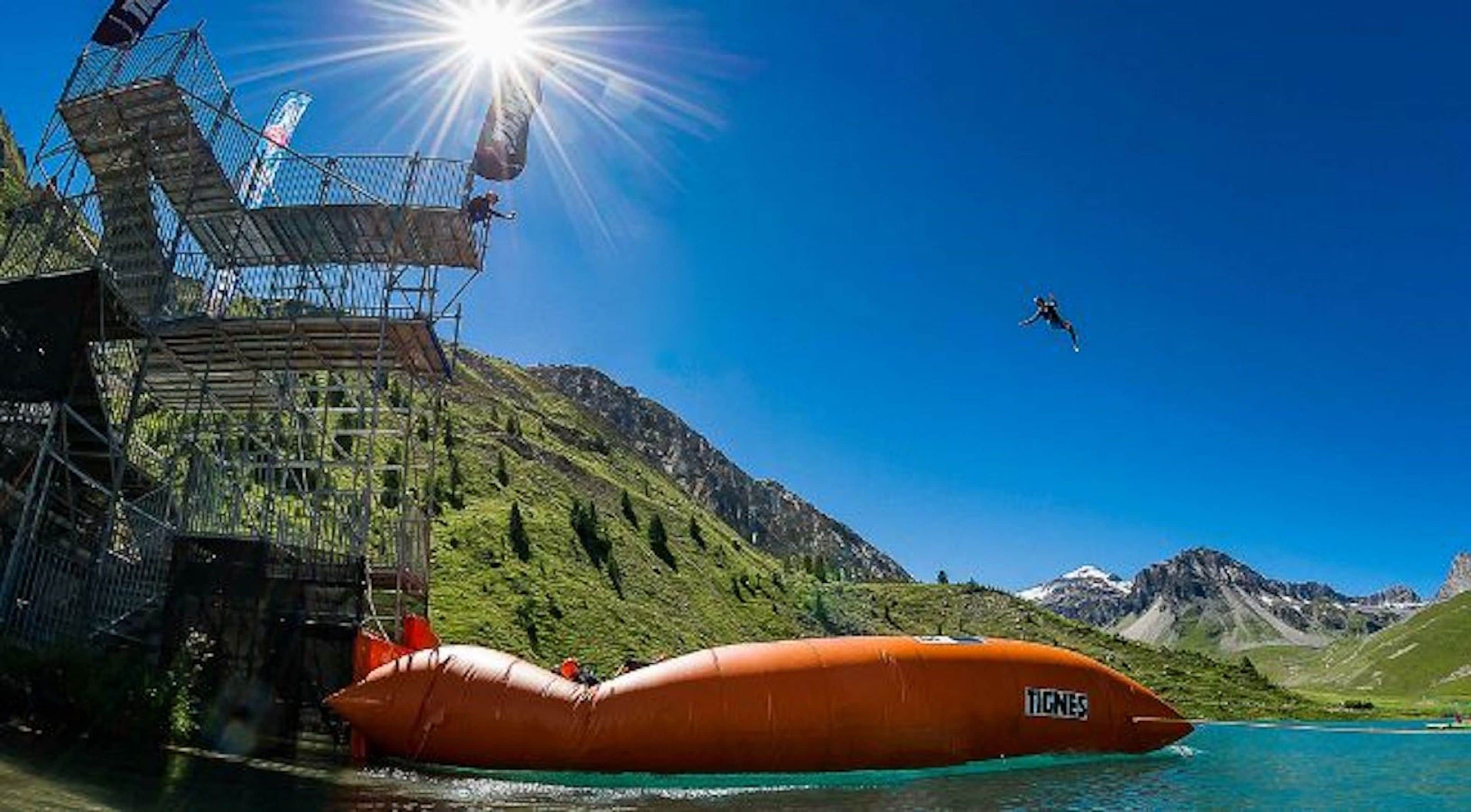 A clear sky, a person skydiving, a large inflatable boat, and a mountainous landscape.