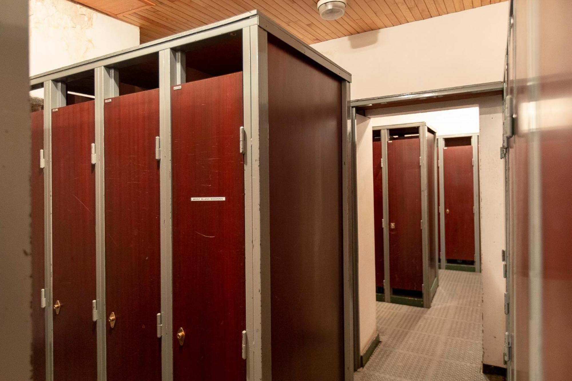 A hallway with multiple wooden doors, some with metal frames, leading to individual rooms.