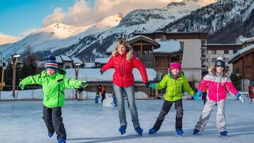 A group of people ice skating in a snowy outdoor area with wooden buildings in the background.