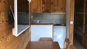 Una cocina compacta con armarios de madera, una pequeña encimera y un comedor con mesa y sillas.