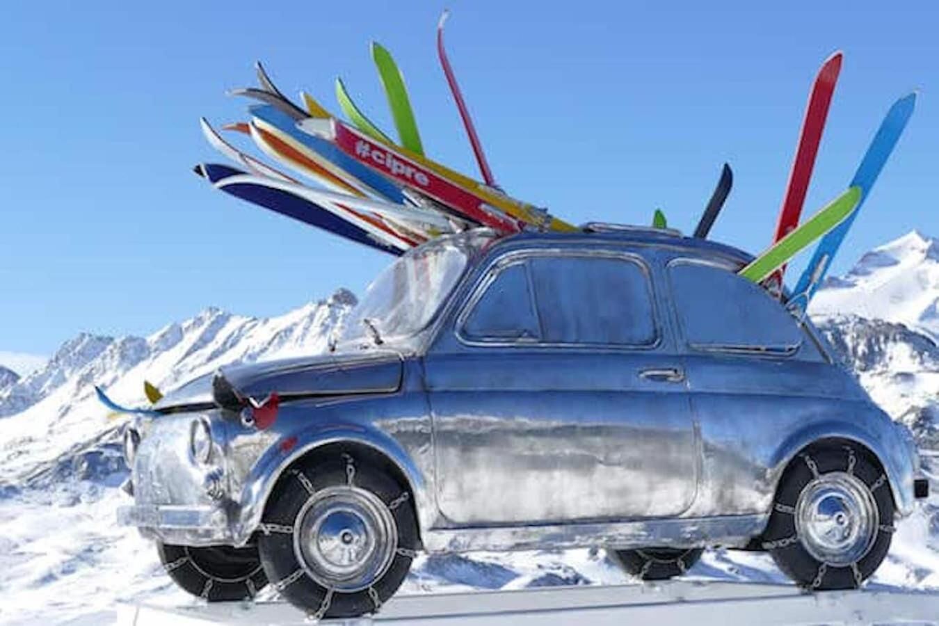 Een oldtimer met ski's op het dak, geparkeerd op een besneeuwde berg.