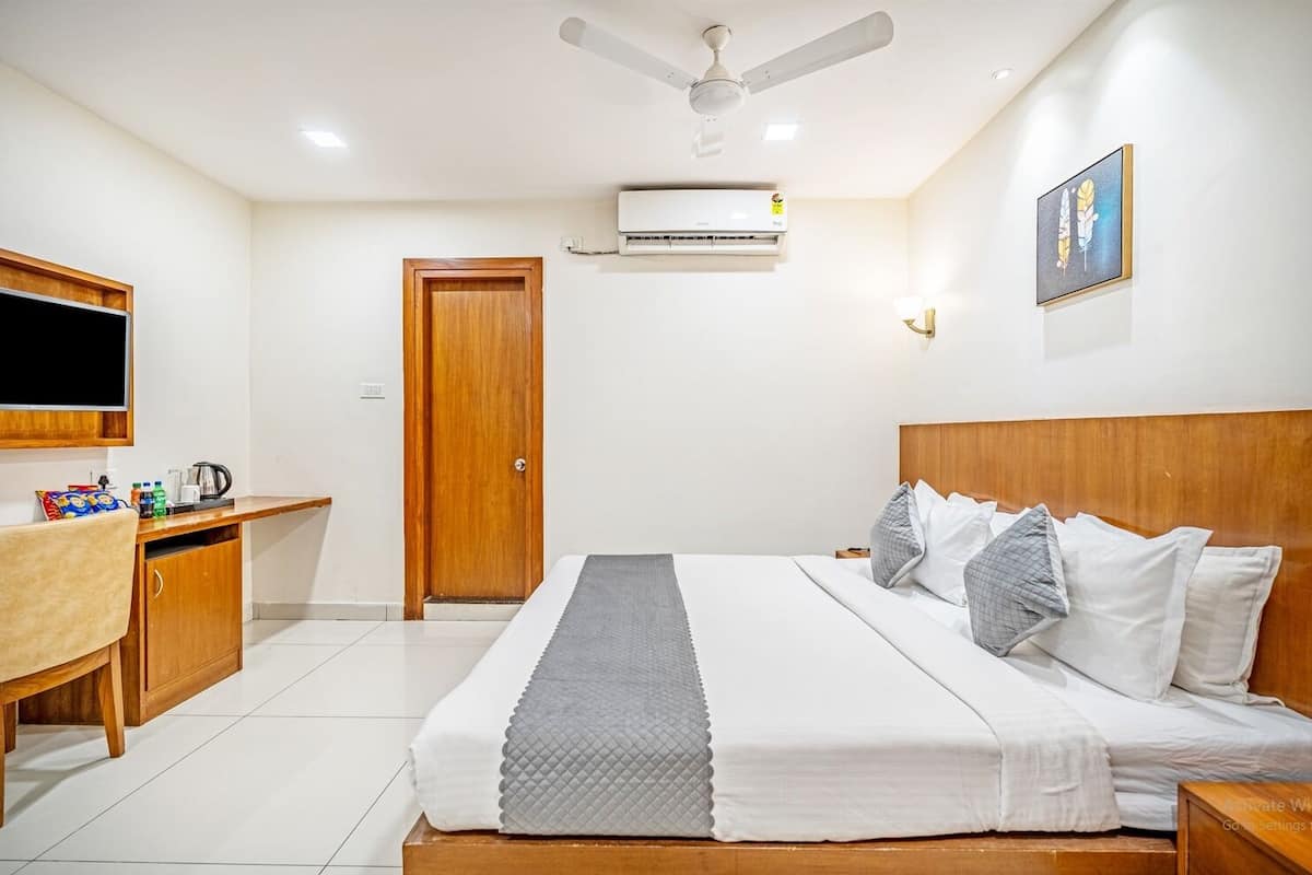 A hotel room with a bed, a desk, a television, and an air conditioning unit.