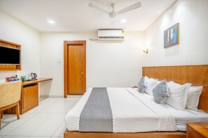 Quarto de hotel com cama, escrivaninha, televisão e ar condicionado.