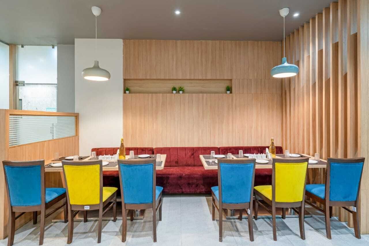 Un coin repas avec un mur en bois, un canapé rouge et des chaises bleues et jaunes.