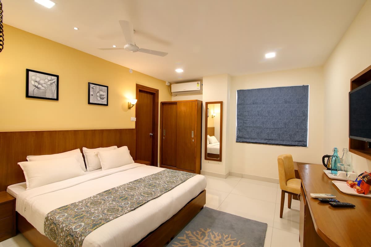 A hotel room with a bed, a desk, a chair, a ceiling fan, and a large window.