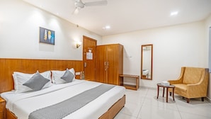 Quarto de hotel com cama grande, armário de madeira, mesa pequena, cadeira e ventoinha no teto.