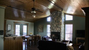 A spacious living area with a stone fireplace, wooden ceiling, and a dining area with a bar. - The Outdoorsman at Homes on Holiday (Ardmore)