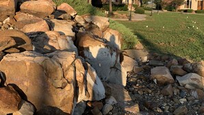 A residential area with large boulders, a grassy lawn, and houses with distinct architectural styles. - The Outdoorsman at Homes on Holiday (Ardmore)