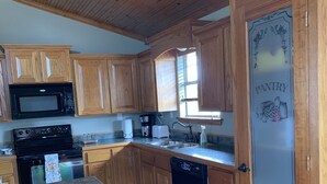 A kitchen with wooden cabinets, a microwave, a stove, a dishwasher, and a pantry door. - The Outdoorsman at Homes on Holiday (Ardmore)