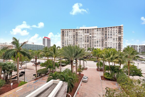A modern hotel with a large parking lot, palm trees, and a clear blue sky.
