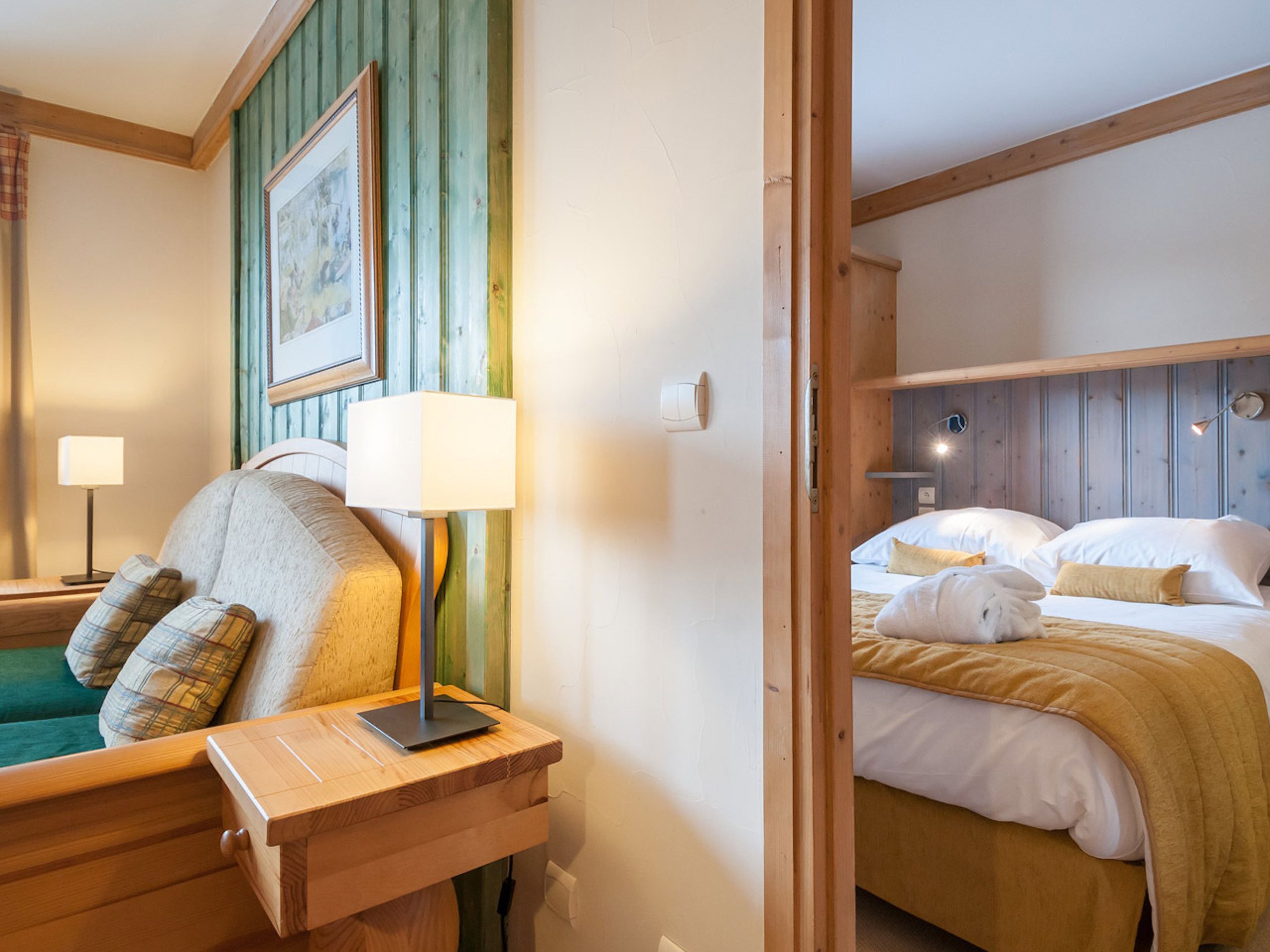 A hotel room with a wooden bed, a bedside table with a lamp, and a green wall with a framed picture.