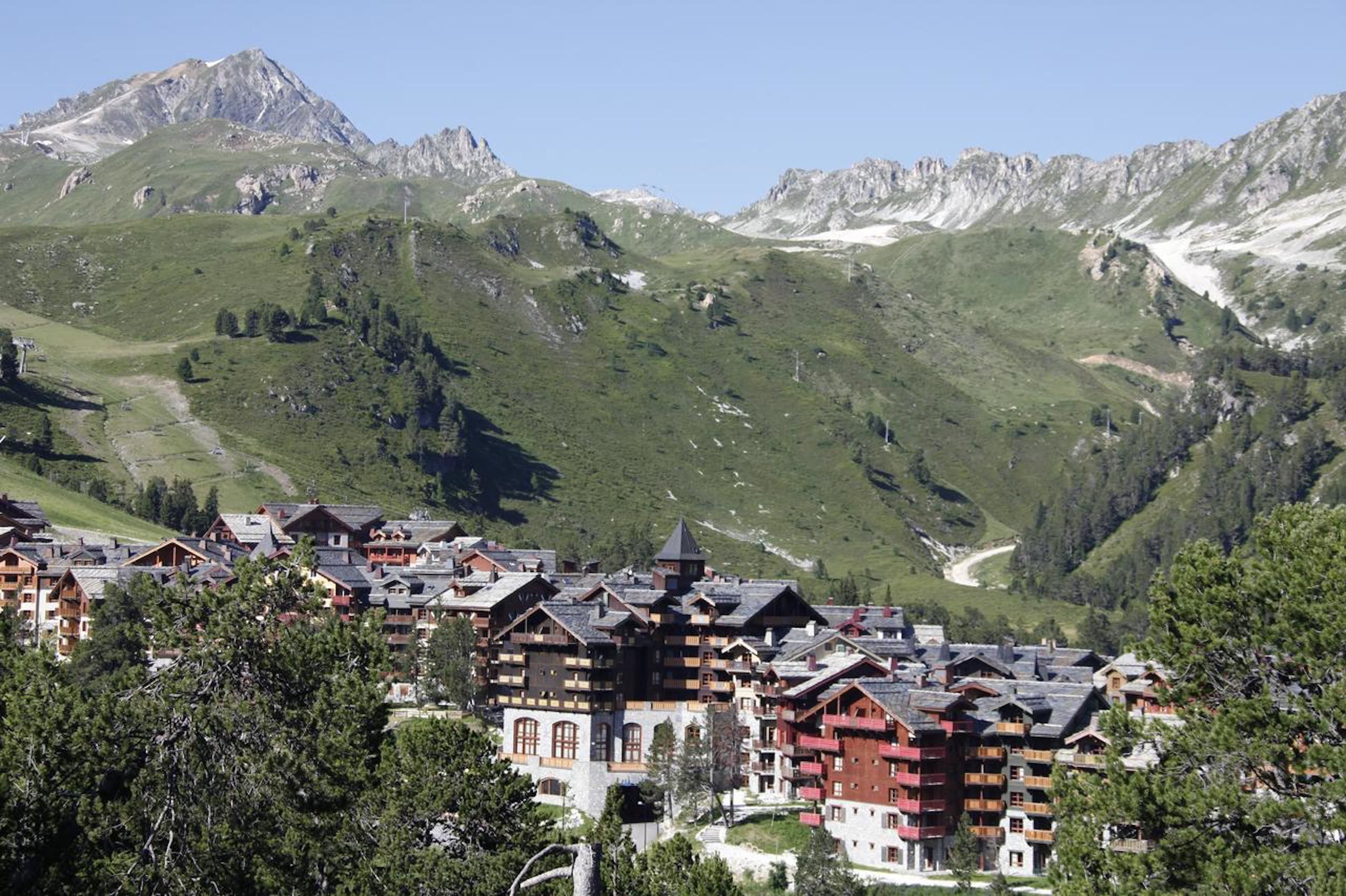 A mountain resort with chalet-style buildings, a ski slope, and a clear view of the surrounding mountains.