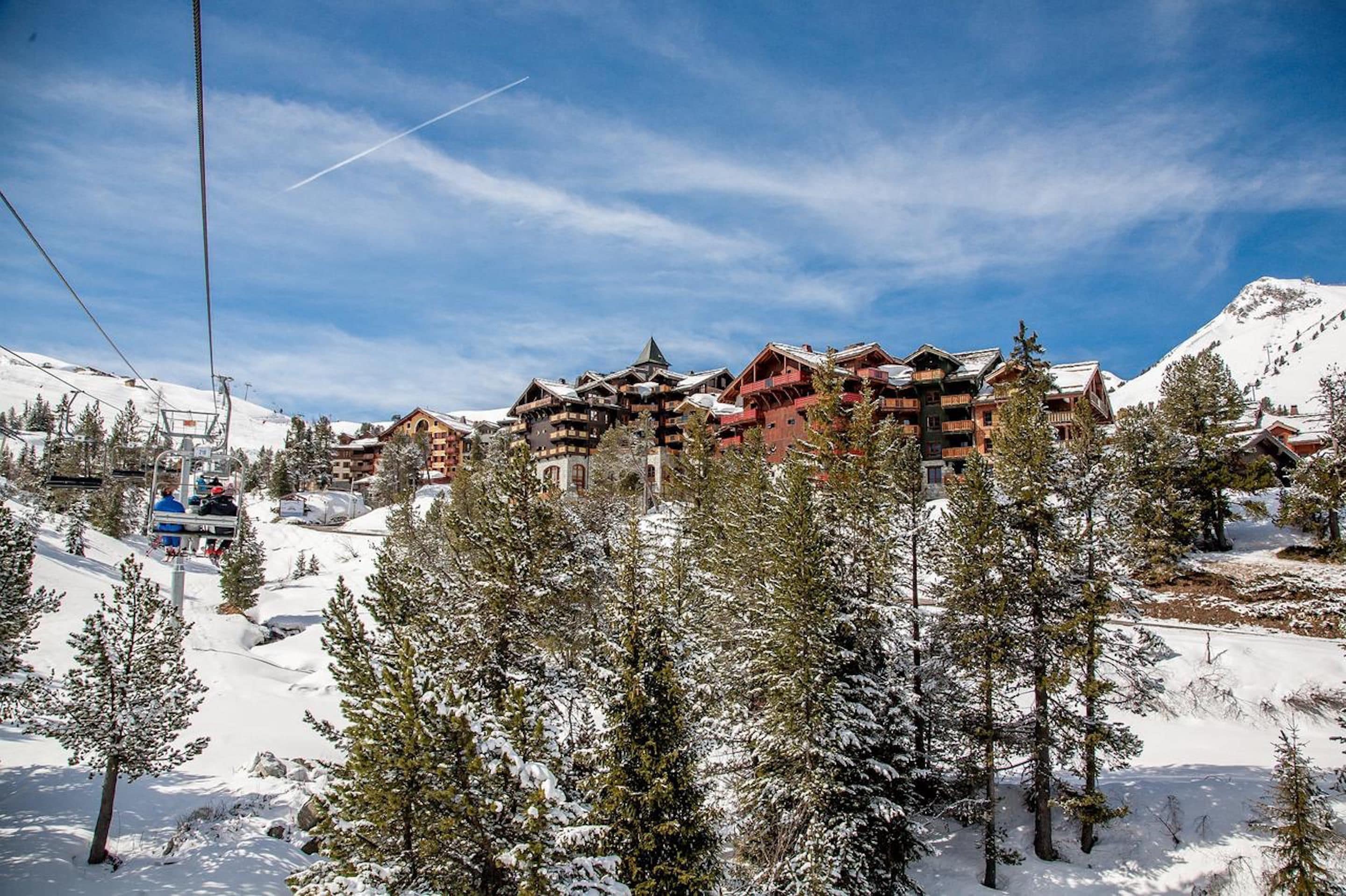 A snow-covered mountain resort with wooden buildings, ski lifts, and trees.