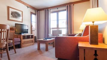 Une chambre d’hôtel équipée d’une télévision, d’un canapé, d’un fauteuil, d’une petite table et d’une lampe.