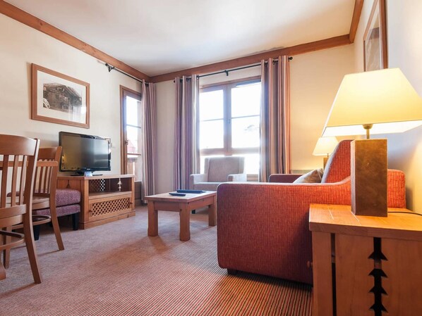 A hotel room with a television, a sofa, a chair, a small table, and a lamp. - Résidence & Spa les Sources de Marie - Arc 1950 Le Village (Bourg-Saint-Maurice)