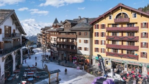 Ein verschneiter Stadtplatz mit traditioneller Architektur, Außenbestuhlung und einem Berg im Hintergrund.