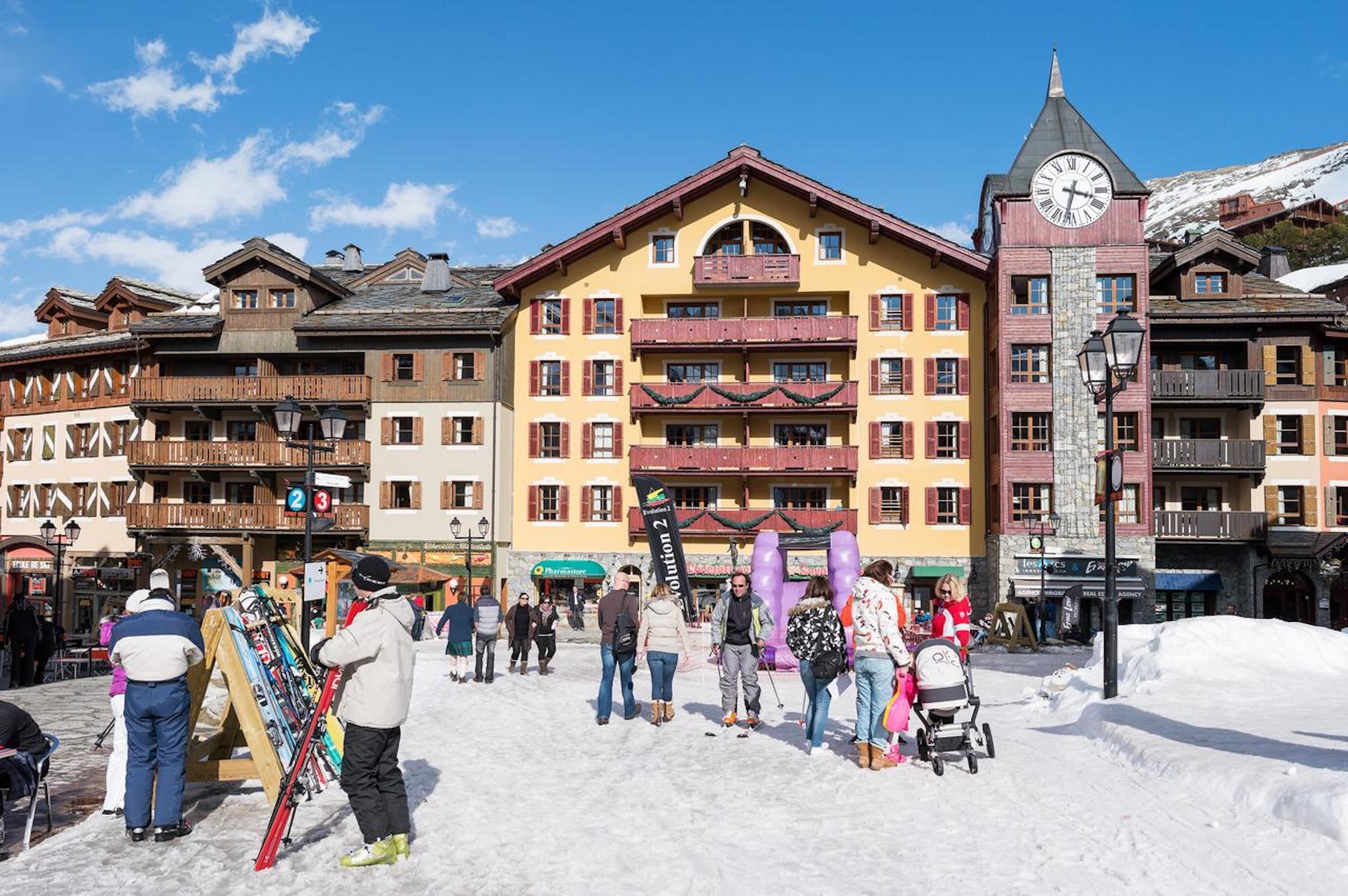 A snow-covered square with a yellow building featuring balconies and a clock tower.