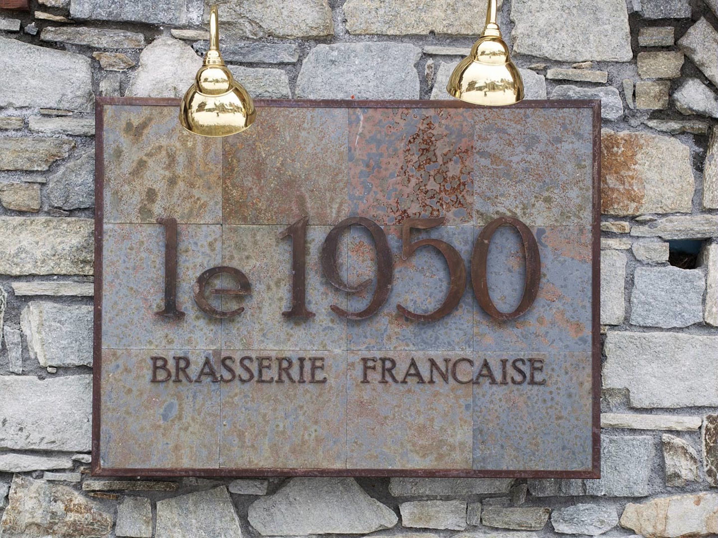 A weathered metal sign with the inscription "le 1950 BRASSERIE FRANCAISE" mounted on a stone wall.