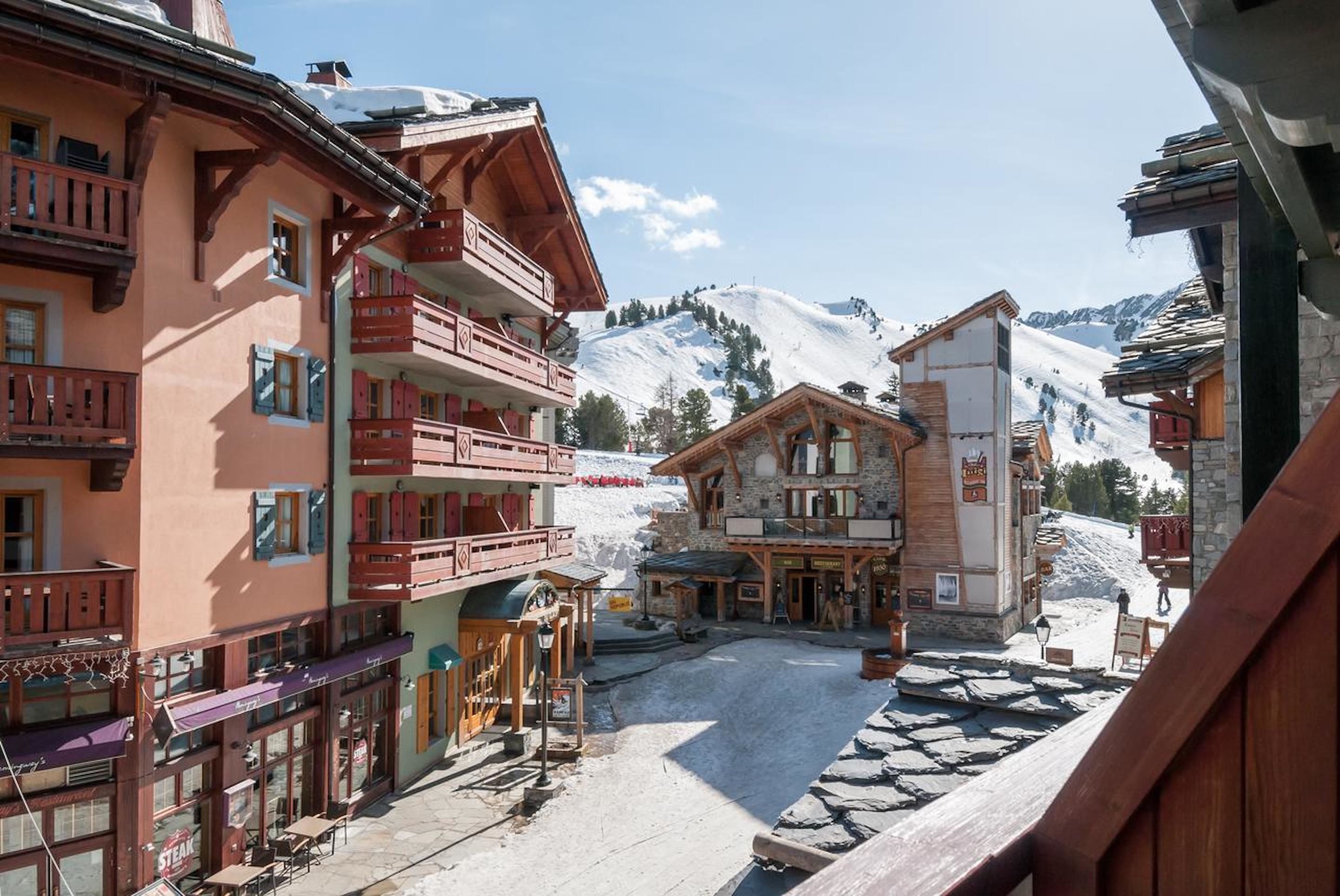 A traditional alpine village with wooden buildings, balconies, and a snow-covered mountain backdrop.