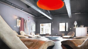 Ein moderner Spa-Raum mit hölzernen Massagestühlen, einem Tisch in der Mitte und großen Fenstern mit Blick auf die Stadt.