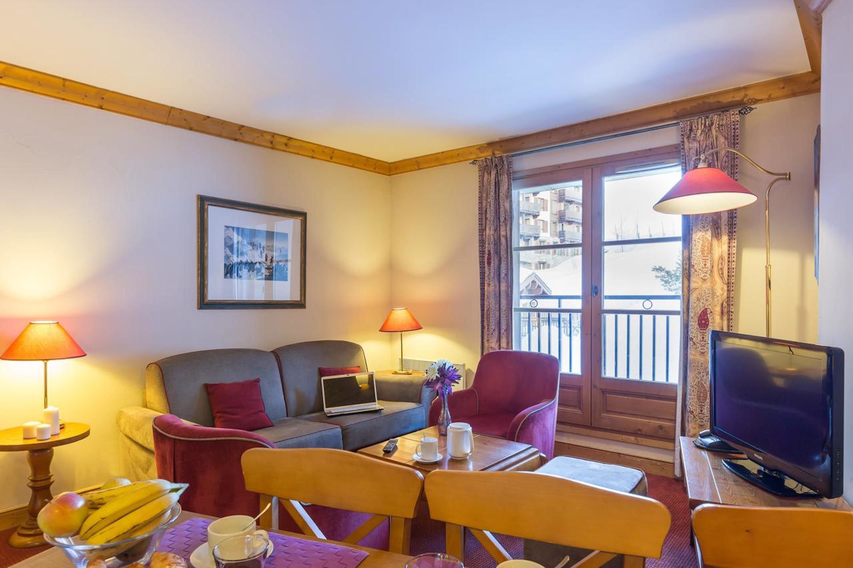 Una habitación de hotel acogedora con sofá, sillones, una mesa de comedor, televisor y un balcón con vistas.