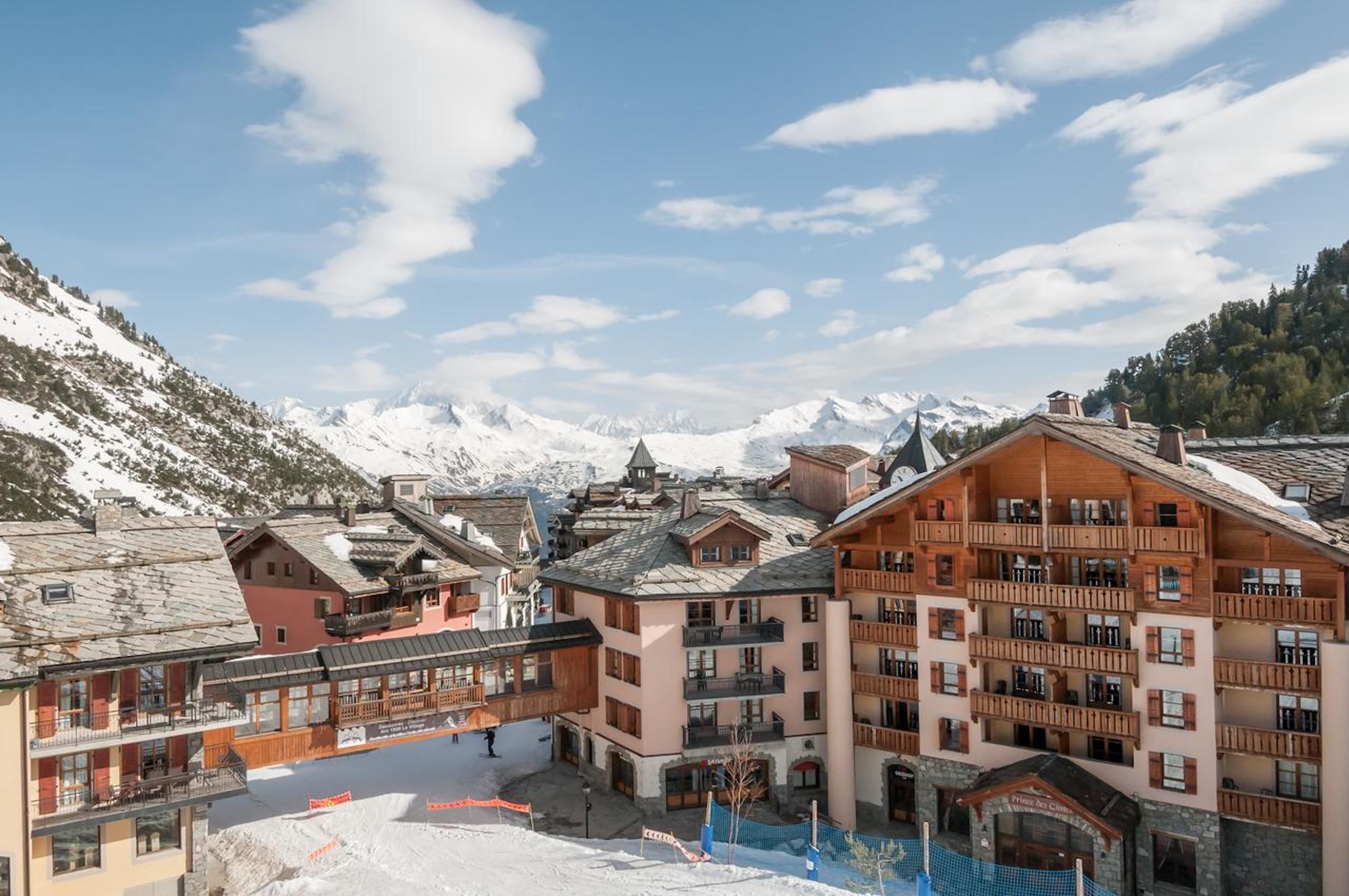 A snow-covered mountain town with traditional wooden buildings, a ski slope, and a clear blue sky.