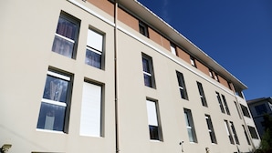 Een meerhoog gebouw met een platte gevel, meerdere ramen en een helderblauwe lucht.