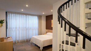 A hotel room with a bed, a desk, a window with curtains, and a staircase. - SG Costa BCN Apartments (Castelldefels)