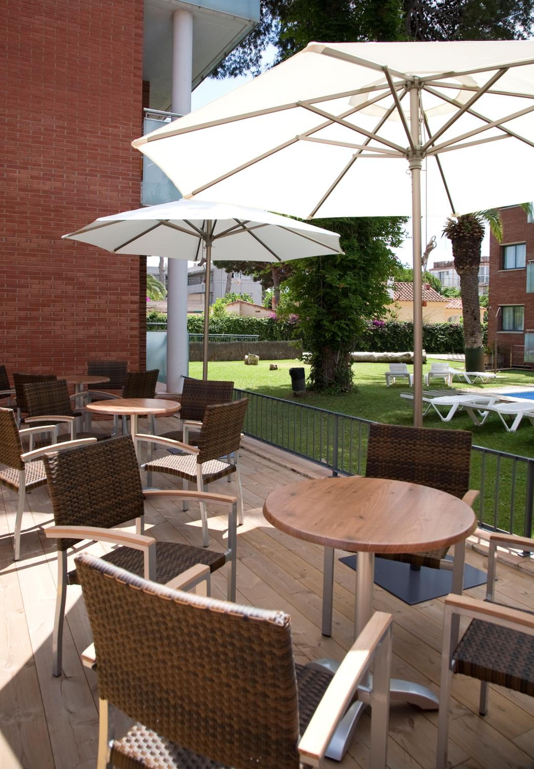 Een terras buiten met ronde tafels en rieten stoelen, omgeven door witte parasols.
