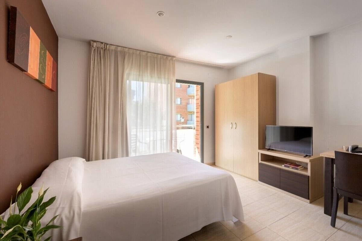 A hotel room with a bed, a TV on a wooden stand, a desk, and a wardrobe.